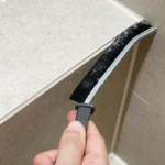 Hand reinigt mit der schmalen Fugenbürste eine schmale Fliesenfuge im Badezimmer