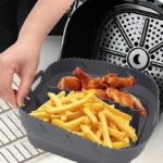 Quadratische Silikoneinlage für die Heißluftfritteuse mit Trennwand, gefüllt mit Pommes und Hühnerflügeln