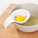 Eiertrenner hält ein Eigelb über einer Schüssel auf einem Holzschneidbrett