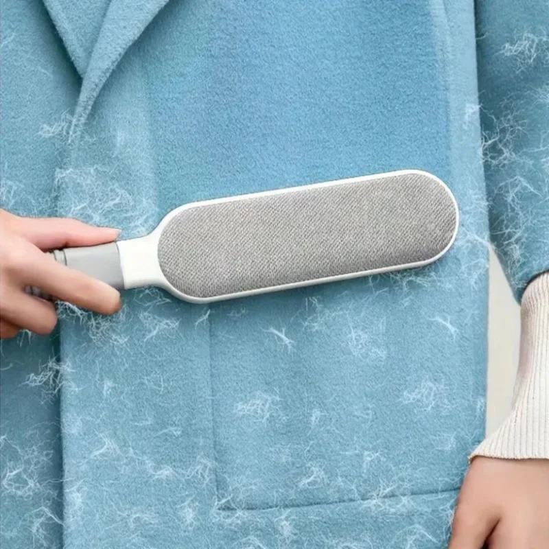 Hand verwendet die Tierhaarbürste an einem blauen Wollmantel voller Haare