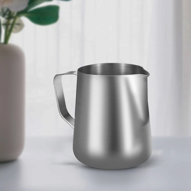 Milchkännchen aus Edelstahl auf einem Tisch neben einer Vase mit Pflanze