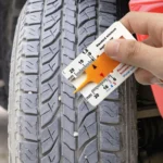 Hand hält den Profiltiefenmesser an einen Autoreifen, um das Profil zu prüfen
